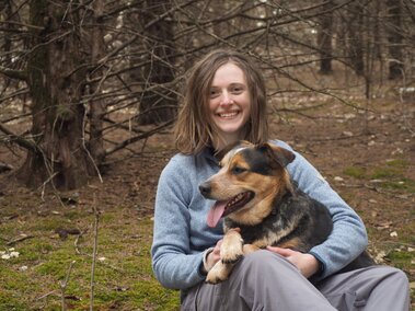 Rachel Rusten poses with her dog in front of trees.